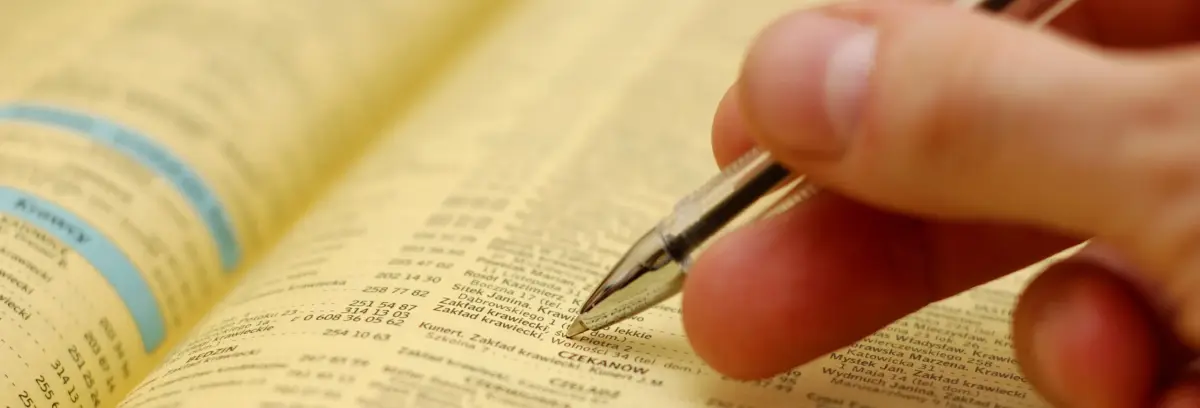 Person using pen on Yellow Pages Data Scraping directory to extract business contact information